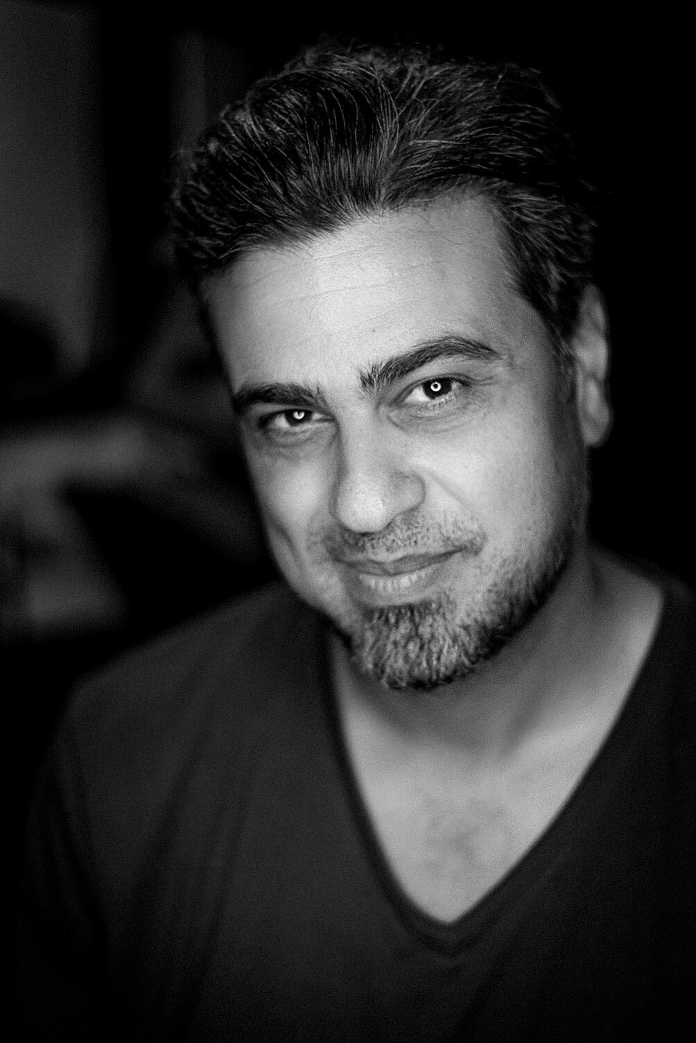 Black-and-white headshot of Arash Afshar with a confident, relaxed expression—positioned as both artist and collaborator.